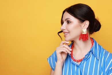 Young woman wearing stylish earrings and necklace on orange background. Space for text