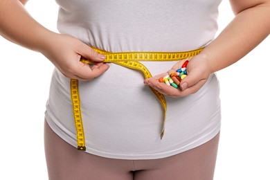 Photo of Plus size woman measuring waist with tape and holding pile of weight loss supplements on white background, closeup