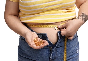 Photo of Plus size woman measuring waist with tape and holding pile of weight loss supplements on white background, closeup