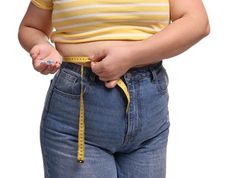 Photo of Plus size woman measuring waist with tape and holding pile of weight loss supplements on white background, closeup