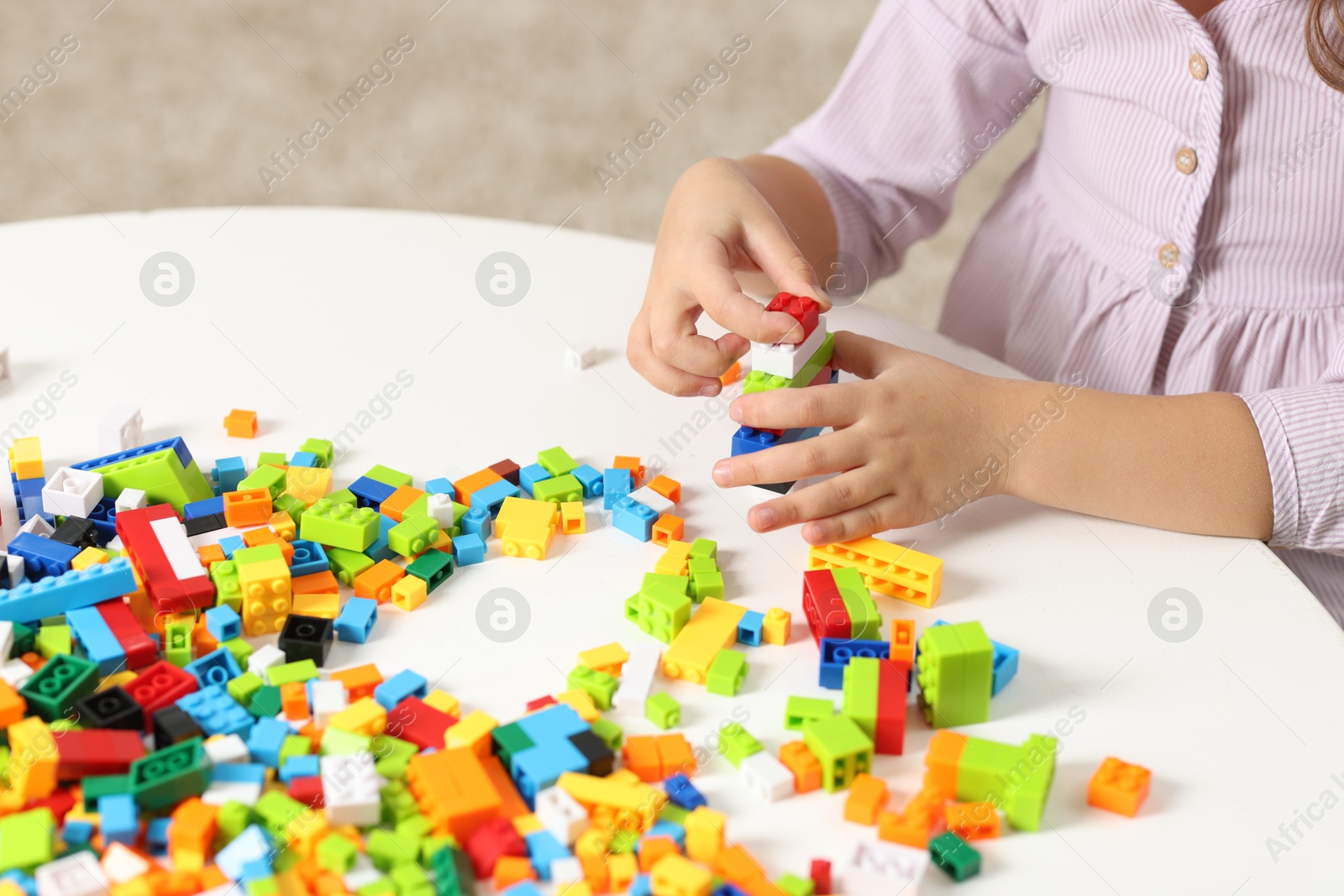 Photo of Girl playing with building blocks at white table indoors, closeup