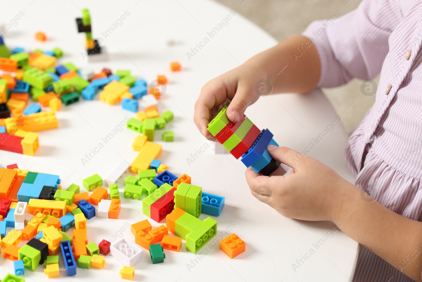 Photo of Girl playing with building blocks at white table indoors, closeup