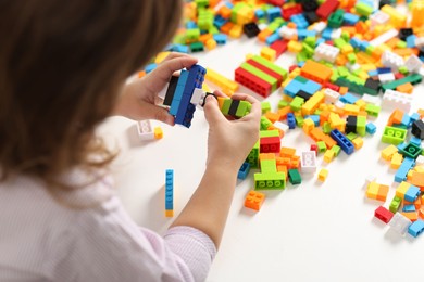 Photo of Girl playing with building blocks at white table indoors, closeup