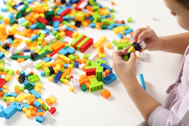 Photo of Girl playing with building blocks at white table indoors, closeup