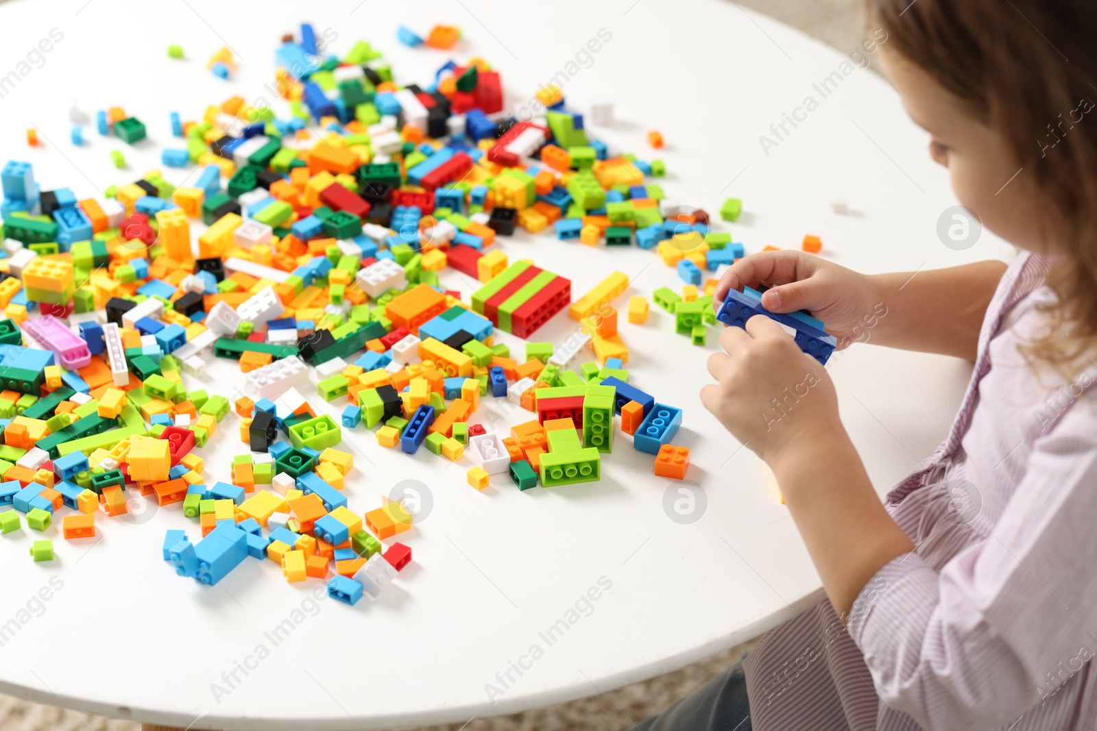 Photo of Girl playing with building blocks at white table indoors, closeup