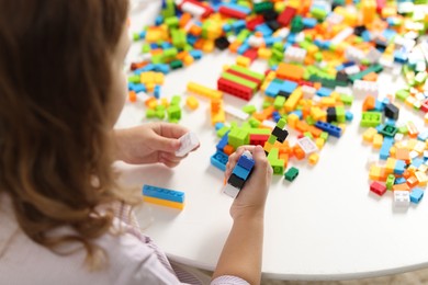 Photo of Girl playing with building blocks at white table indoors, closeup