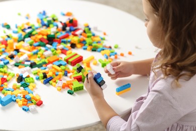 Photo of Girl playing with building blocks at white table indoors, closeup