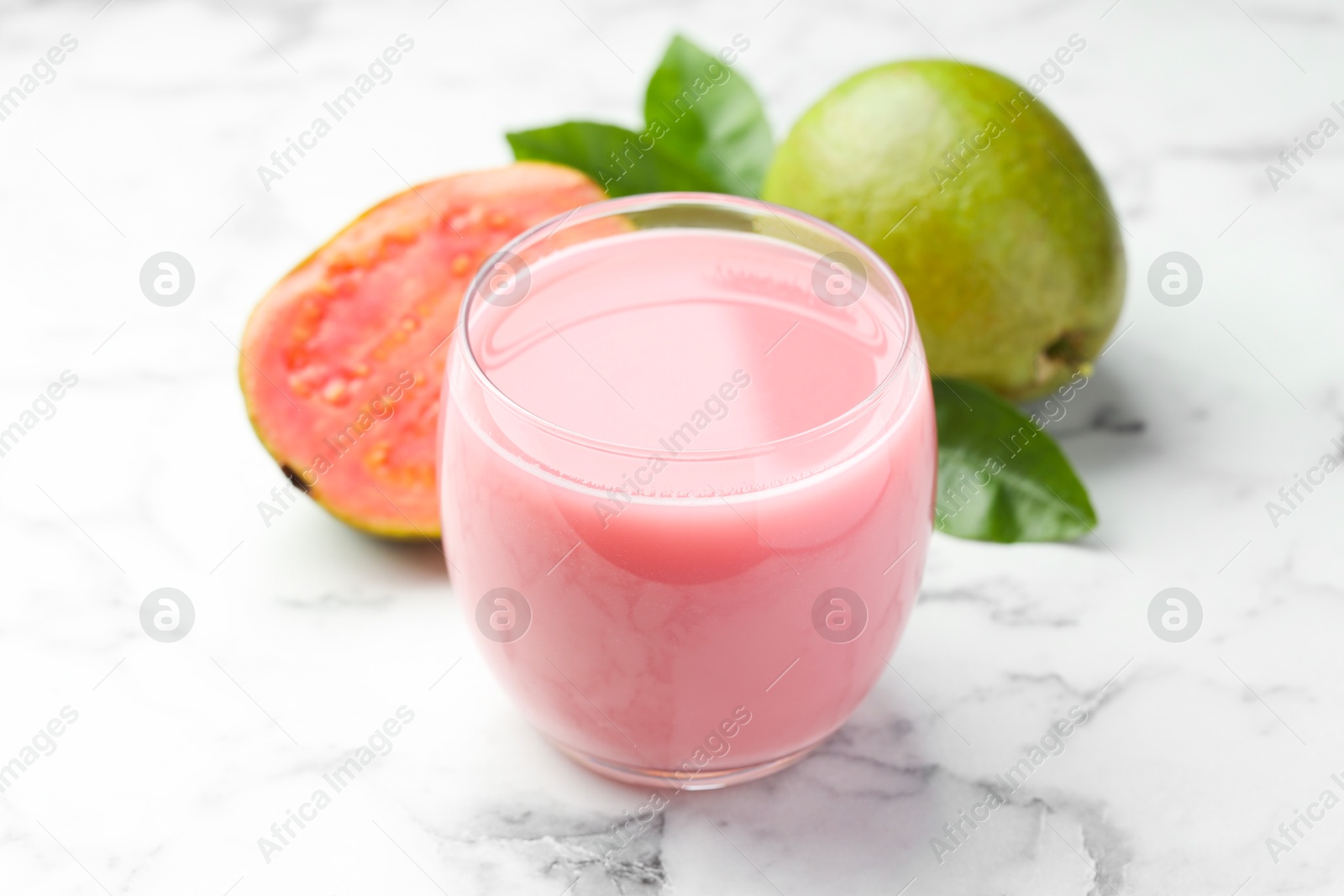 Photo of Tasty guava juice in glass, leaves and fruits on white marble table, closeup