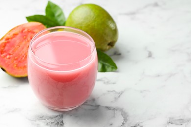 Photo of Tasty guava juice in glass, leaves and fruits on white marble table, closeup. Space for text