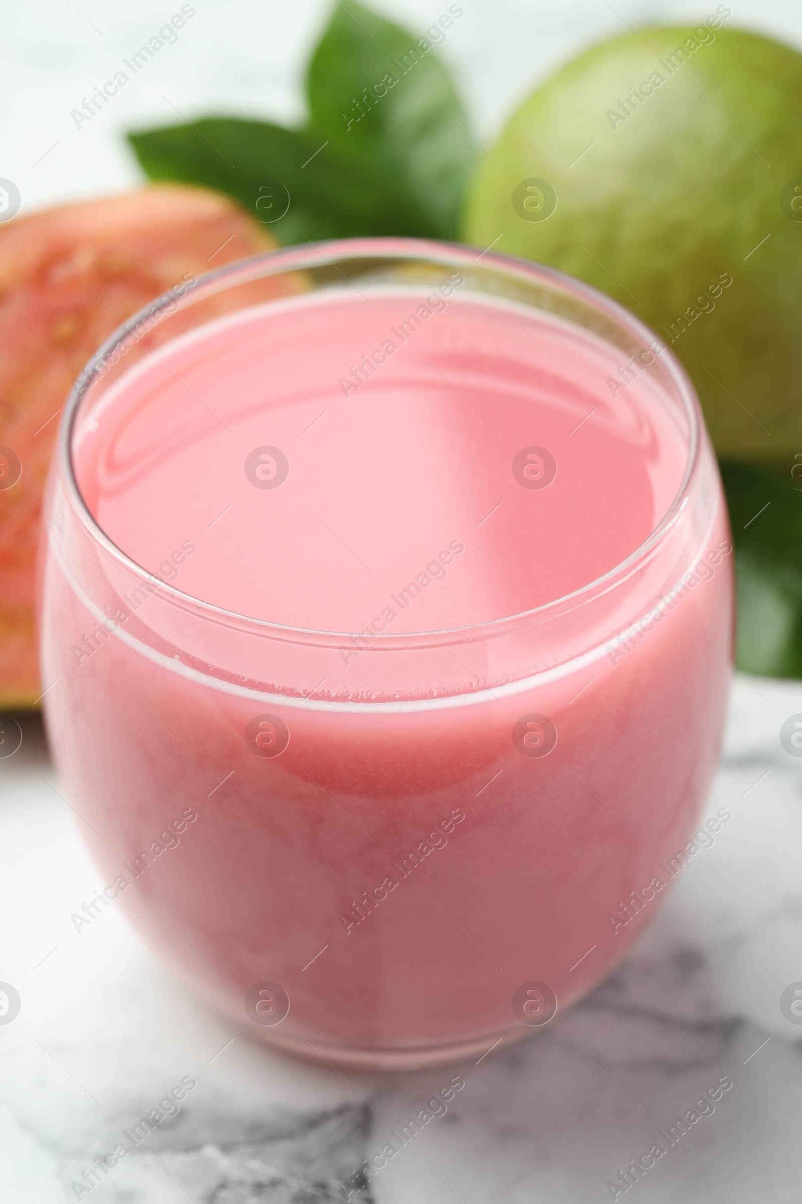 Photo of Tasty guava juice in glass on white marble table, closeup