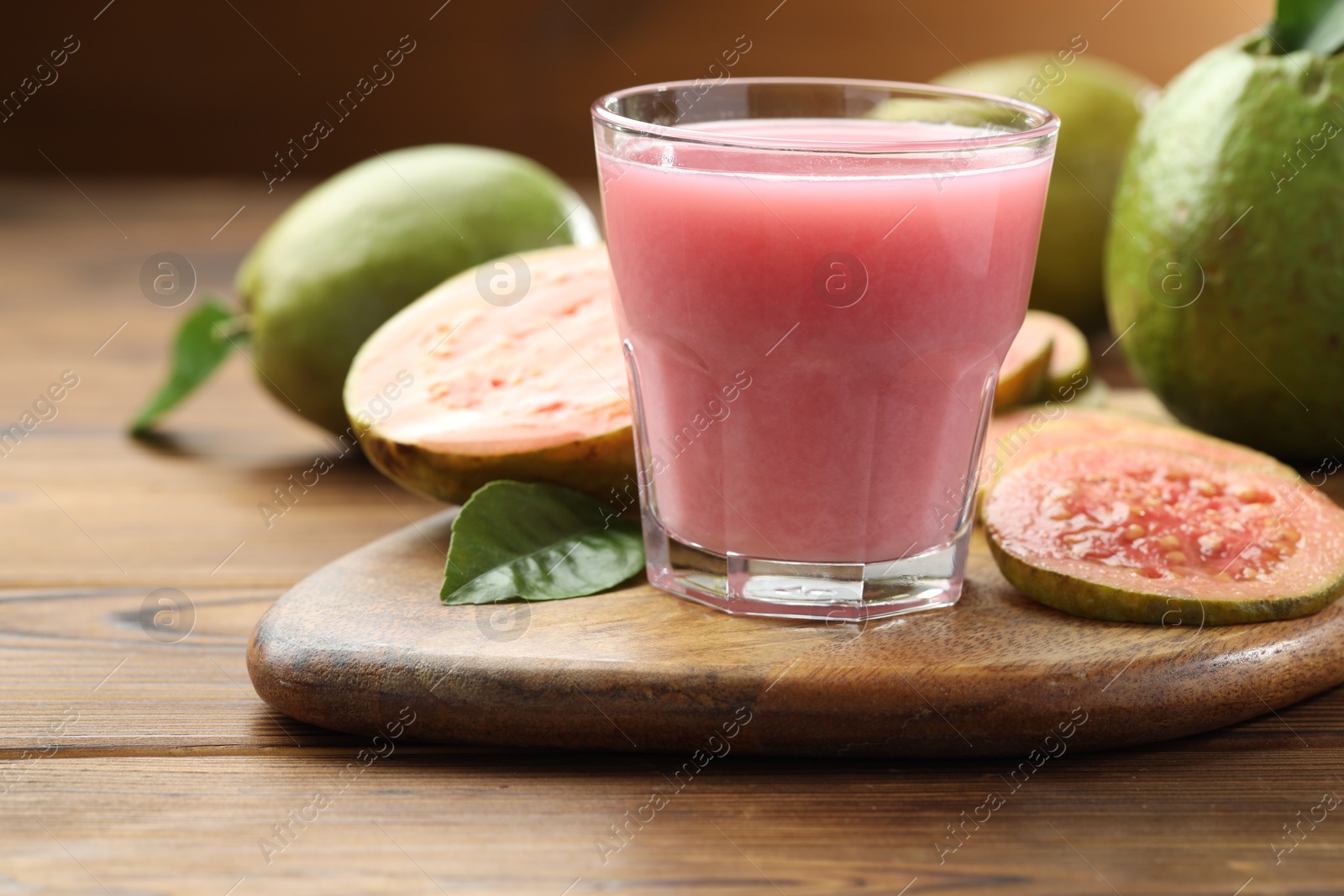 Photo of Tasty guava juice in glass, leaves and fruits on wooden table, closeup