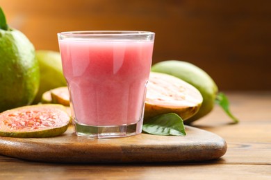 Photo of Tasty guava juice in glass, leaves and fruits on wooden table, closeup