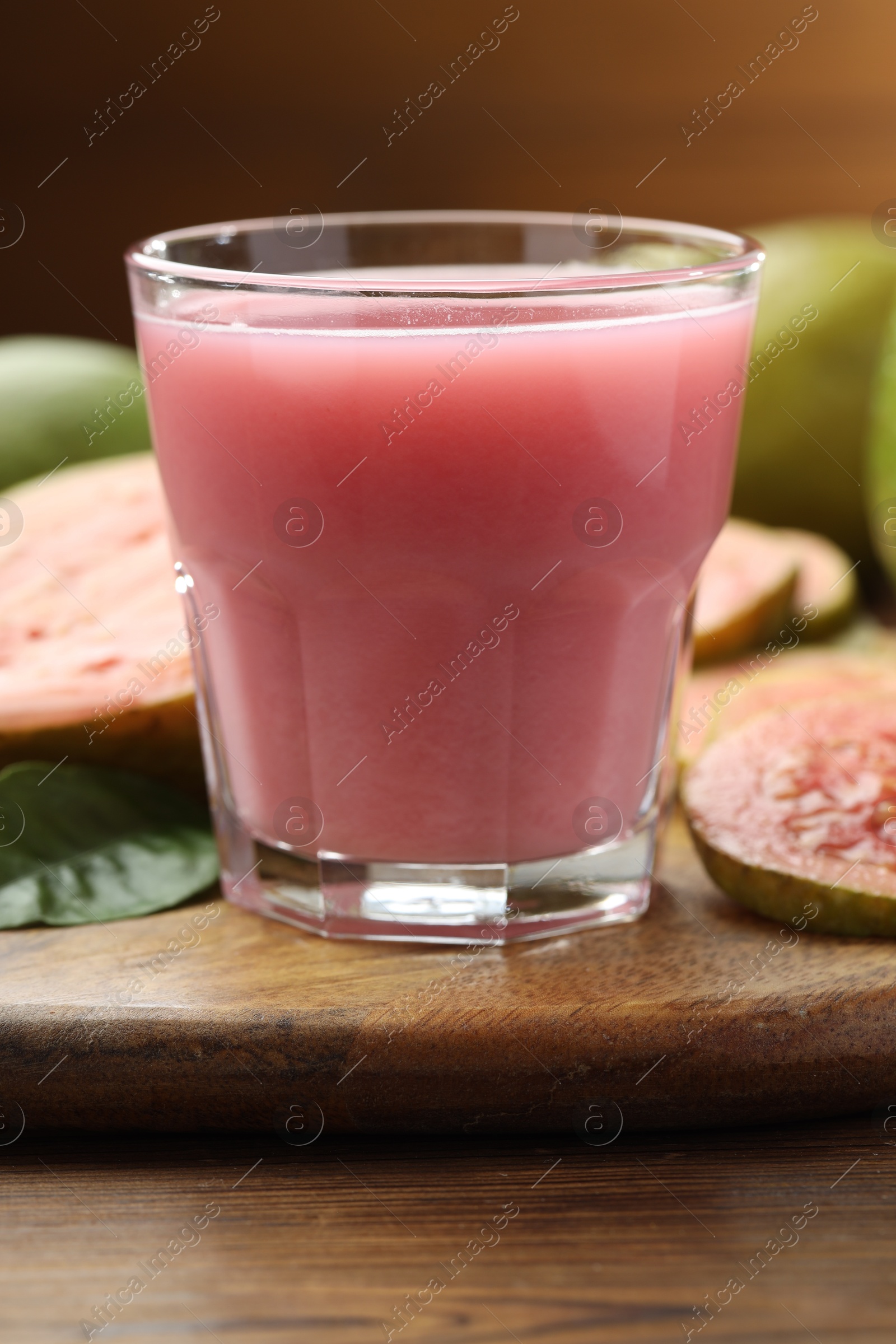 Photo of Tasty guava juice in glass, leaf and fruits on wooden table, closeup