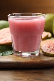 Photo of Tasty guava juice in glass, leaf and fruits on wooden table, closeup