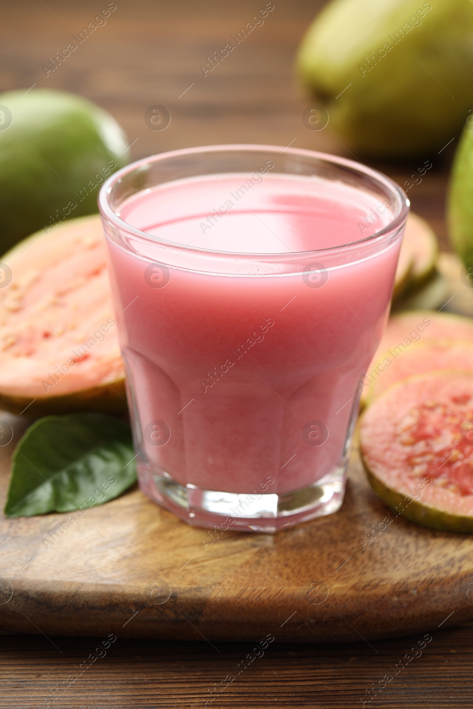 Photo of Tasty guava juice in glass, leaf and fruits on wooden table, closeup