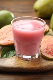 Photo of Tasty guava juice in glass, leaf and fruits on wooden table, closeup