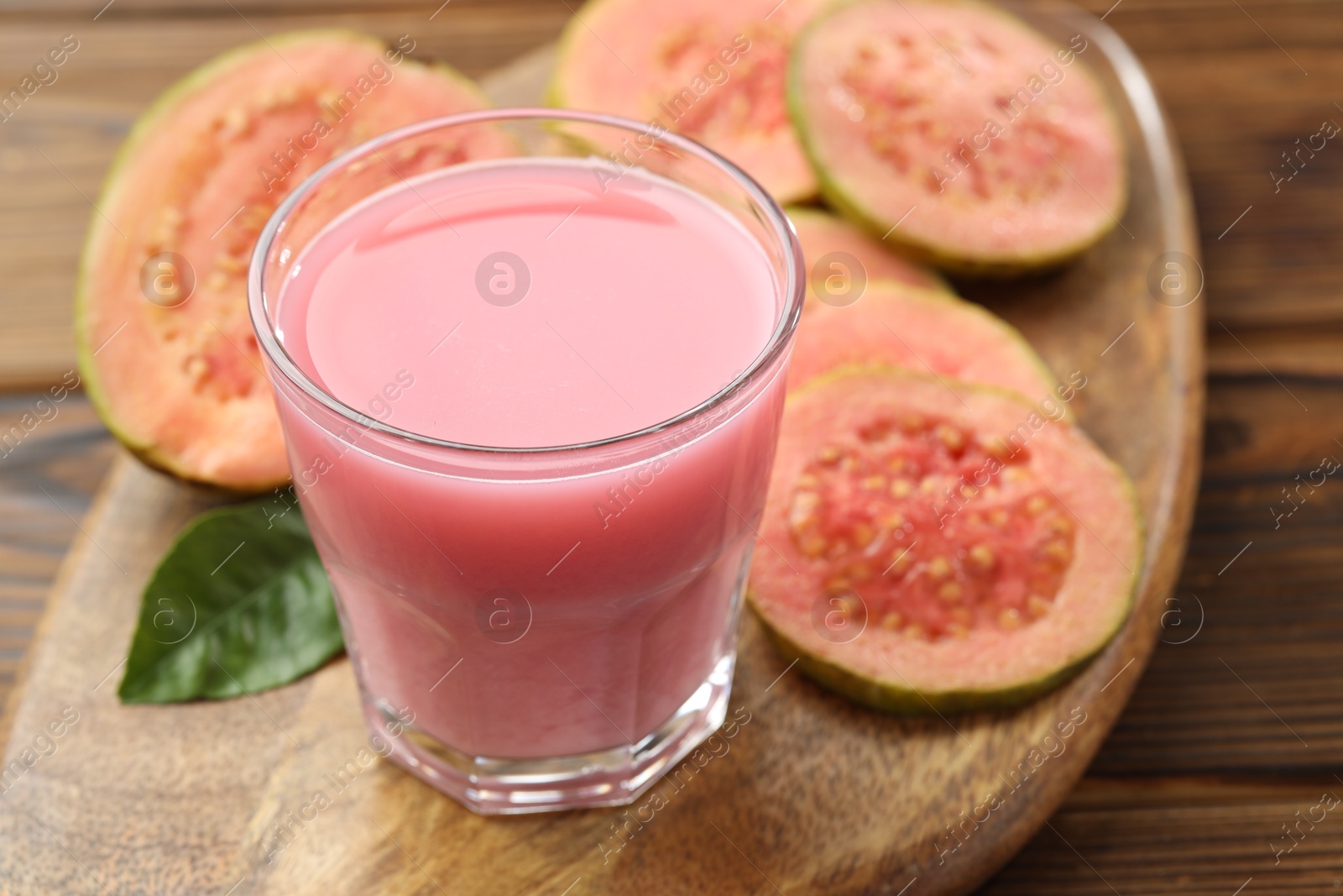 Photo of Tasty guava juice in glass, leaf and slices of fruits on wooden table, closeup