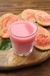 Photo of Tasty guava juice in glass, leaf and slices of fruits on wooden table, closeup