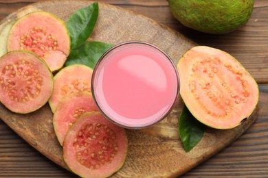 Photo of Tasty guava juice in glass, leaves and slices of fruits on wooden table, flat lay