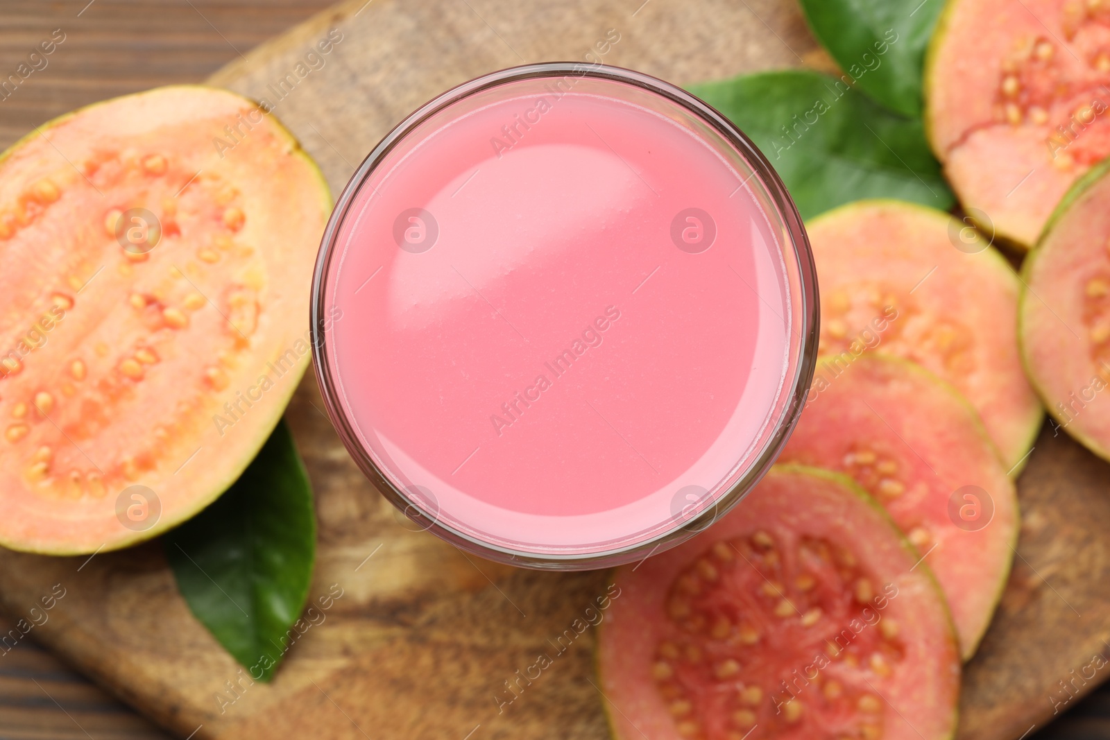 Photo of Tasty guava juice in glass, leaves and slices of fruits on wooden table, top view