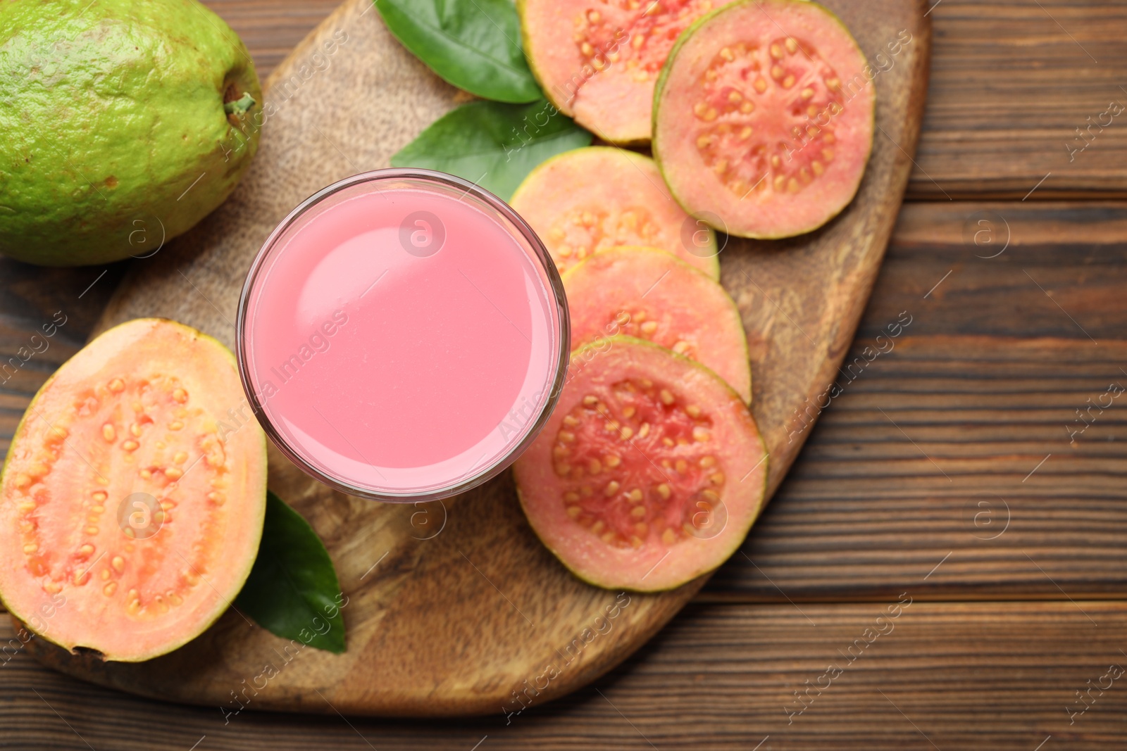 Photo of Tasty guava juice in glass, leaves and slices of fruits on wooden table, flat lay