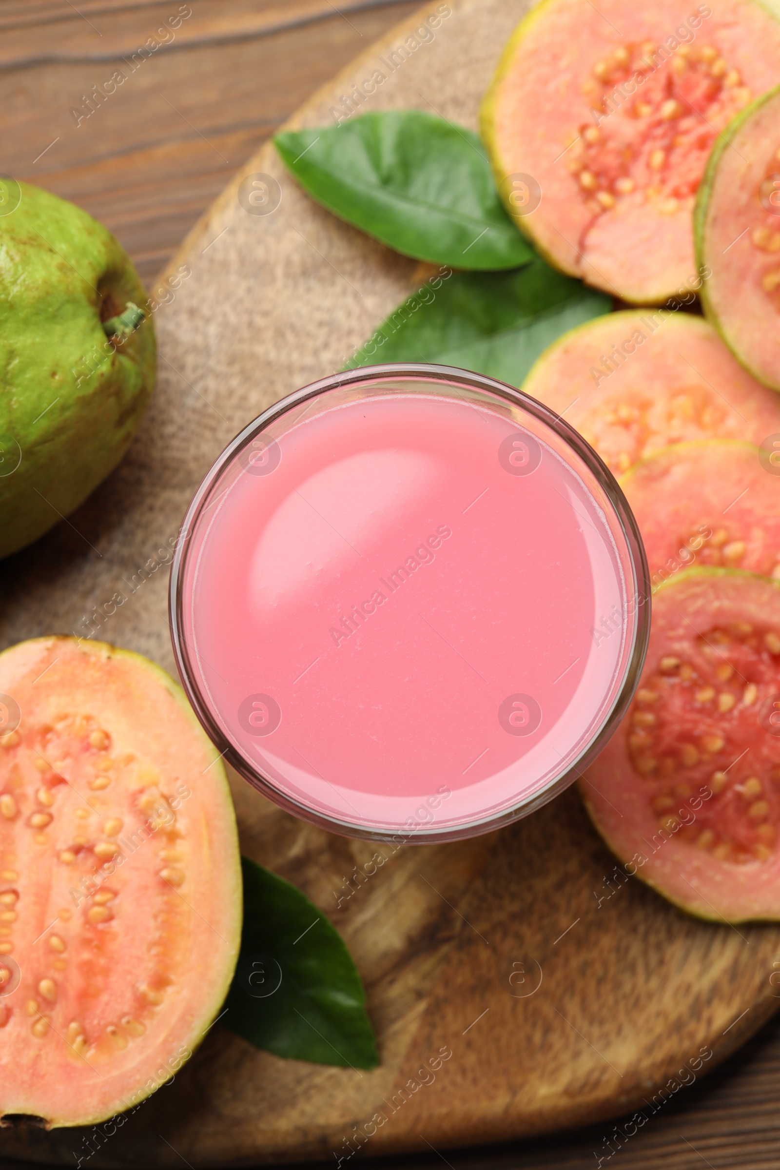 Photo of Tasty guava juice in glass, leaves and slices of fruits on wooden table, flat lay