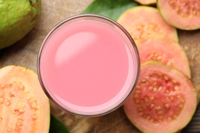 Photo of Tasty guava juice in glass and slices of fruits on wooden table, flat lay