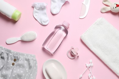 Photo of Baby oil, clothes and bath accessories on light pink background, flat lay