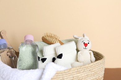 Photo of Baby oil and bath accessories in basket on color background, closeup