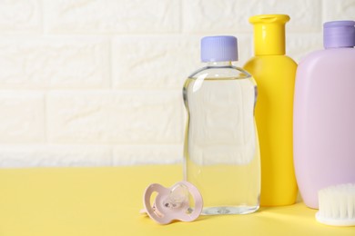 Photo of Baby oil and bath accessories on yellow table. Space for text