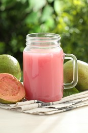 Photo of Tasty guava juice in mason jar and fresh fruits on white table outdoors, closeup