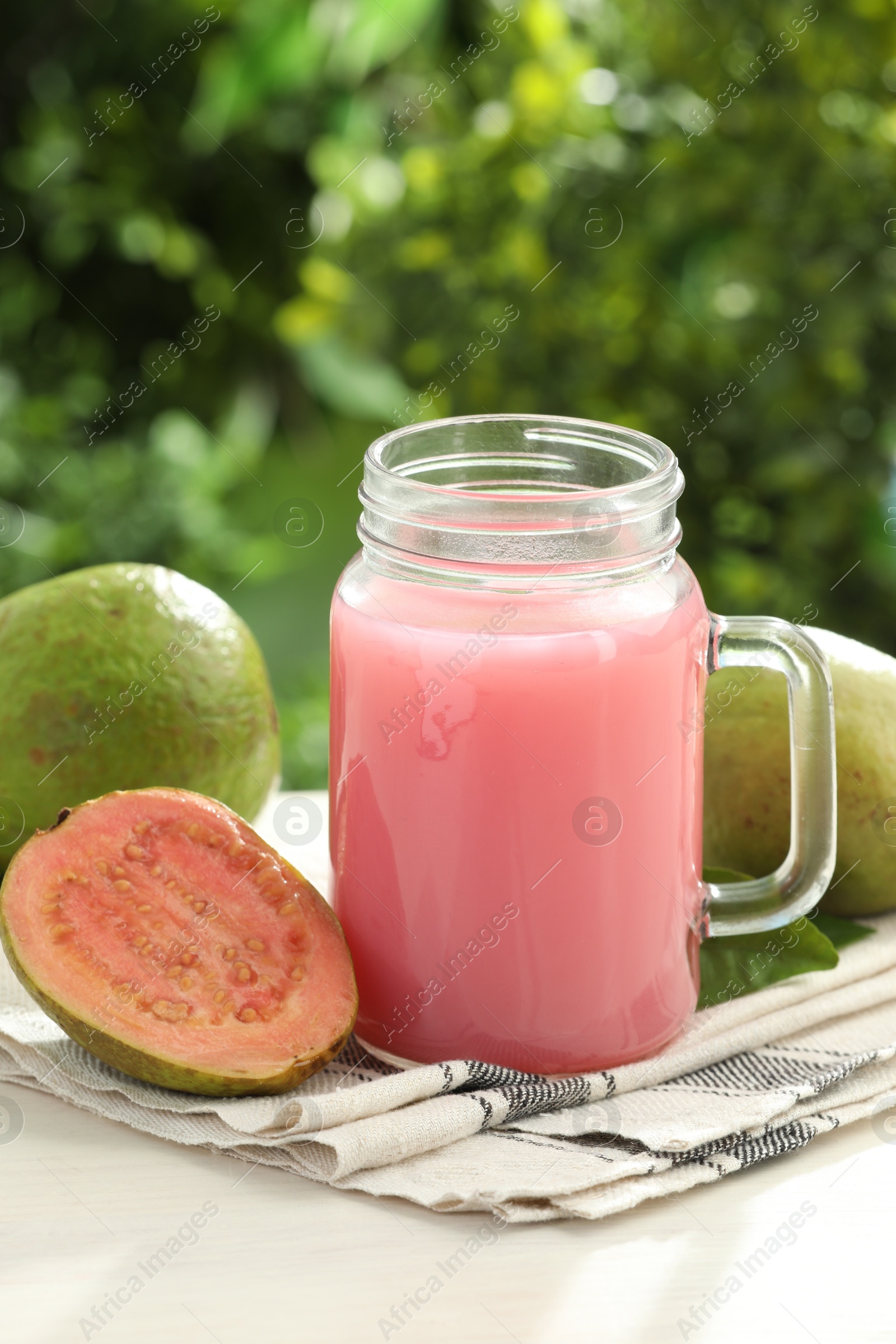 Photo of Fresh guava juice in mason jar on white table outdoors