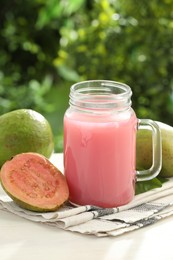 Photo of Fresh guava juice in mason jar on white table outdoors