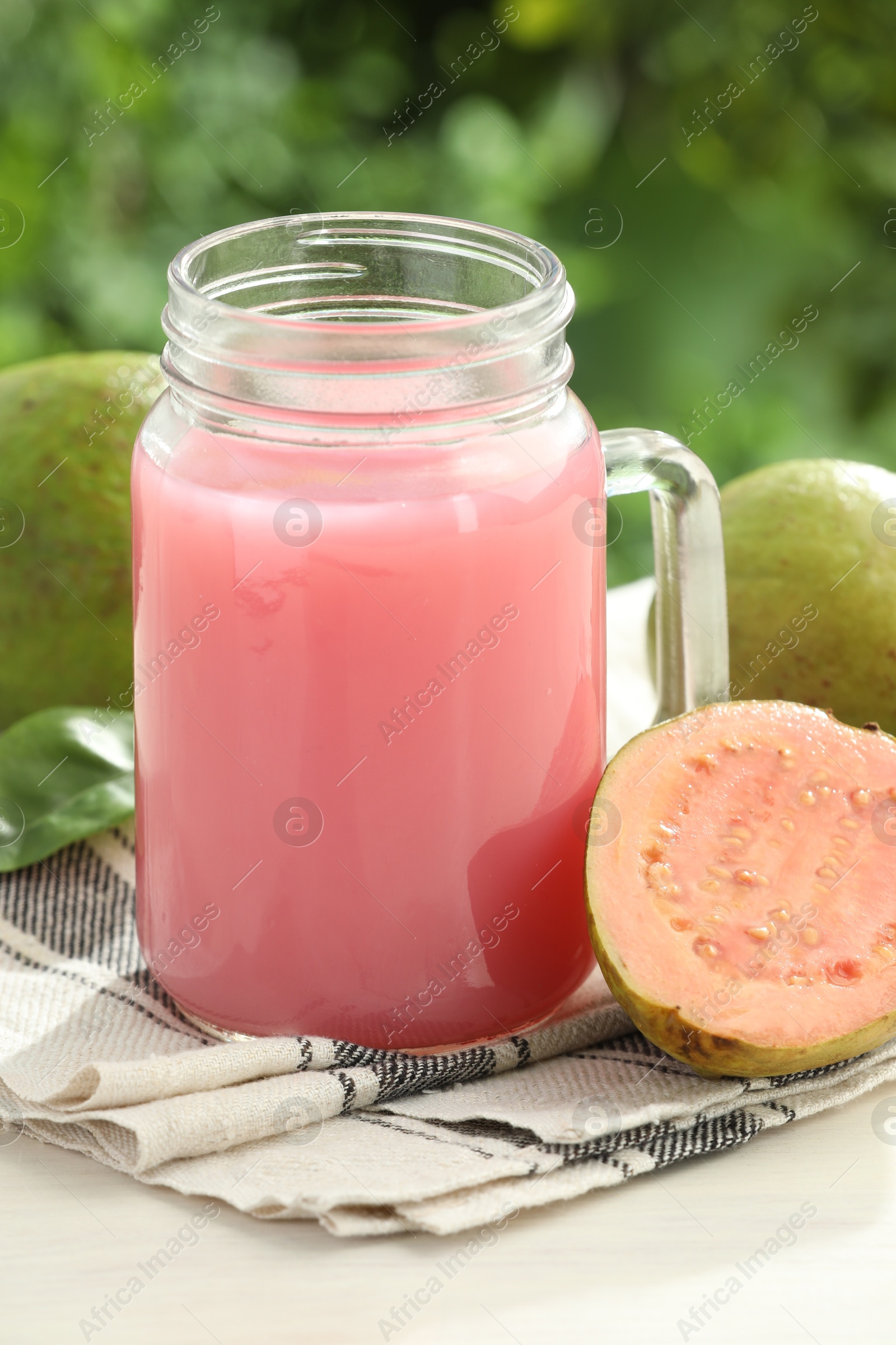 Photo of Tasty guava juice in mason jar and fresh fruits on white table outdoors, closeup