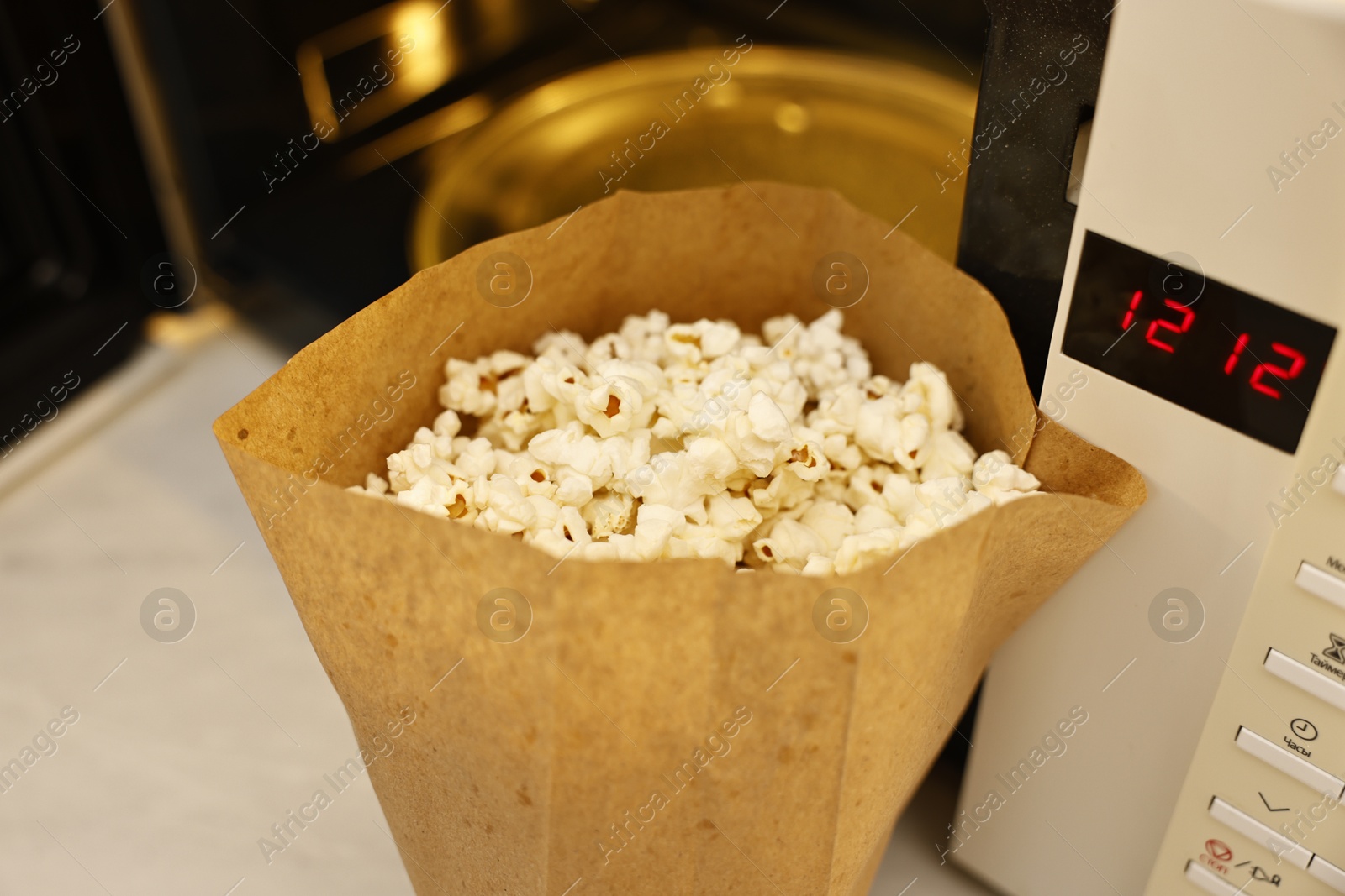 Photo of Tasty popcorn in paper bag near microwave oven on table, closeup