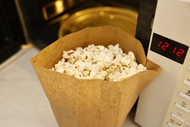 Photo of Tasty popcorn in paper bag near microwave oven on table, closeup