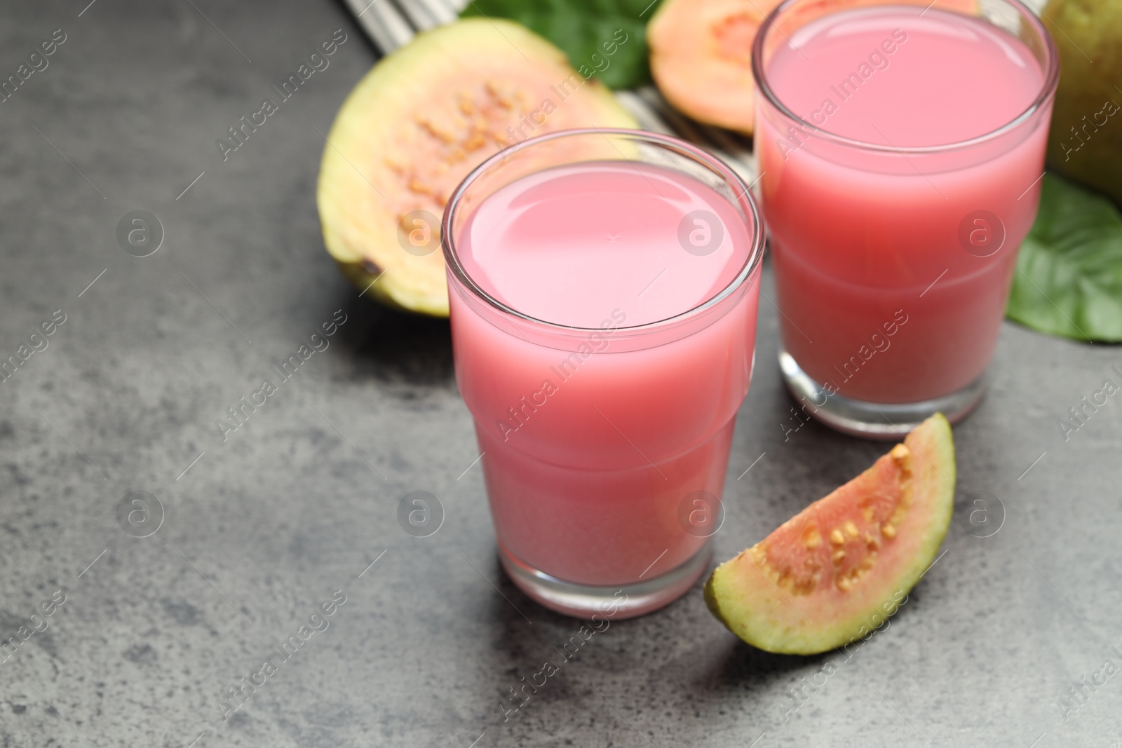 Photo of Refreshing guava juice and fresh fruits on grey table, closeup. Space for text