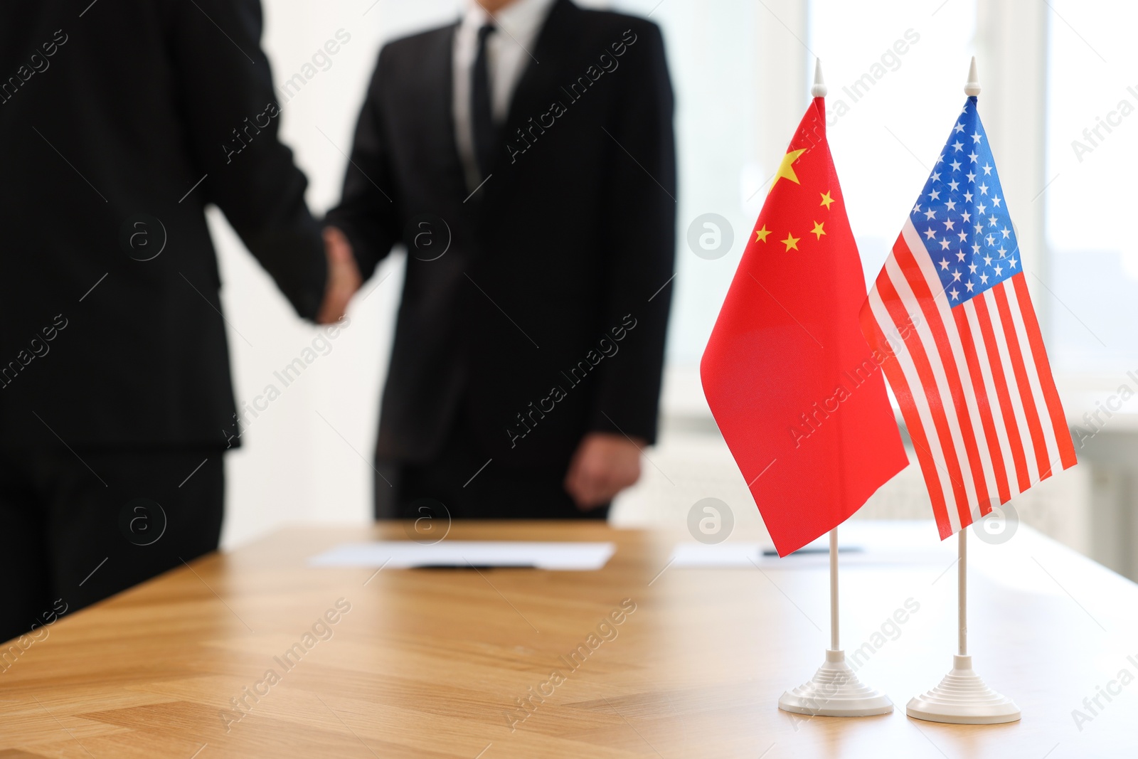 Photo of Diplomats shaking hands during meeting indoors, focus on flags of USA and China