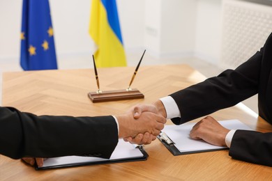 Photo of Diplomats shaking hands during meeting at wooden table indoors, closeup