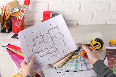 Photo of Designer working with house plan and color selection chart at white table, closeup