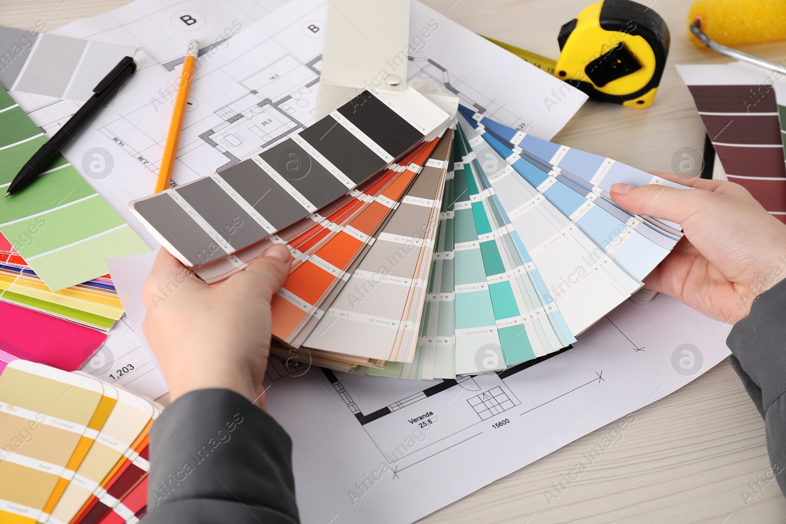 Photo of Designer with color selection chart working at white wooden table, closeup