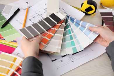 Photo of Designer with color selection chart working at white wooden table, closeup