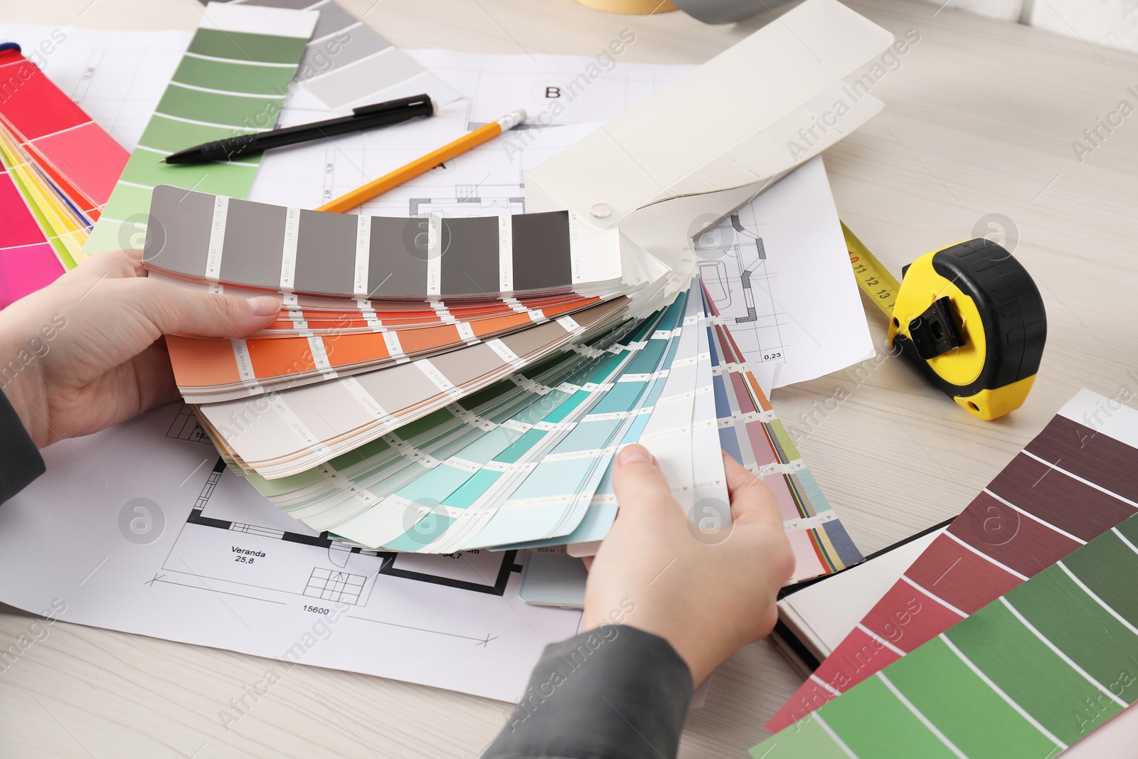 Photo of Designer with color selection chart working at white wooden table, closeup