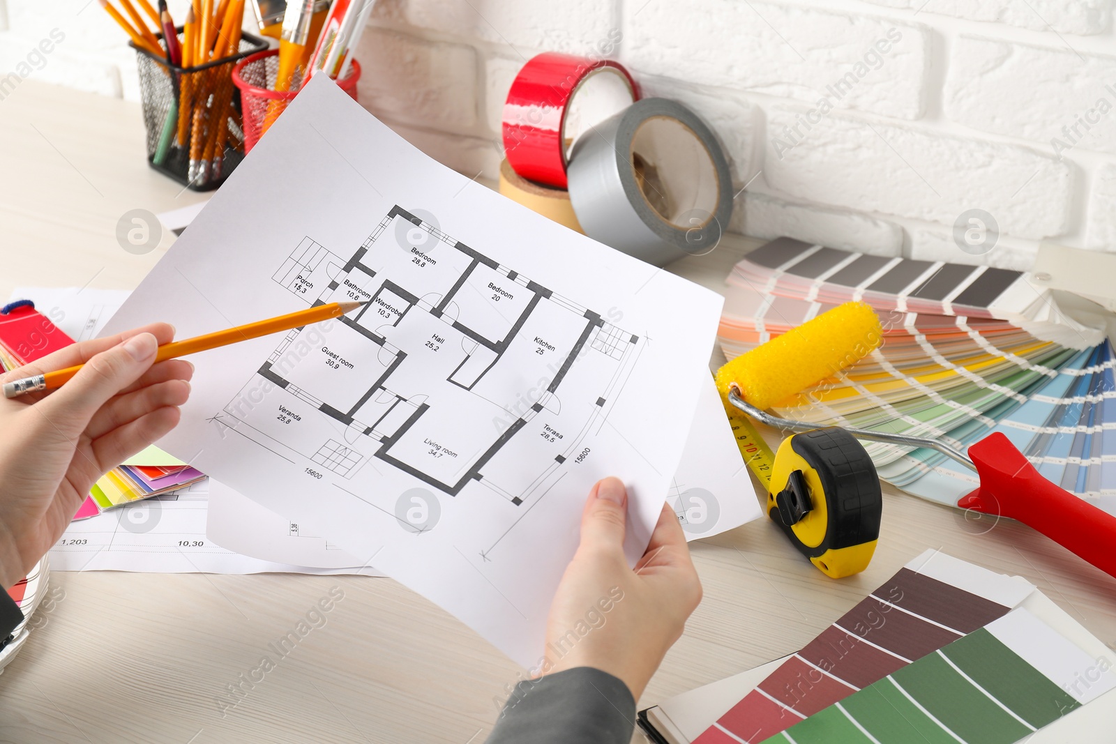 Photo of Designer working with house plan at white wooden table, closeup