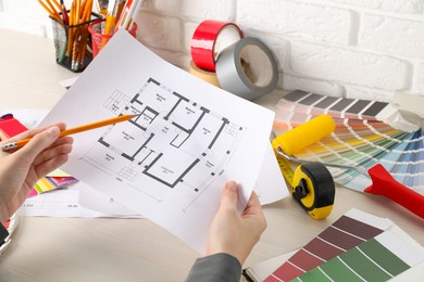 Photo of Designer working with house plan at white wooden table, closeup