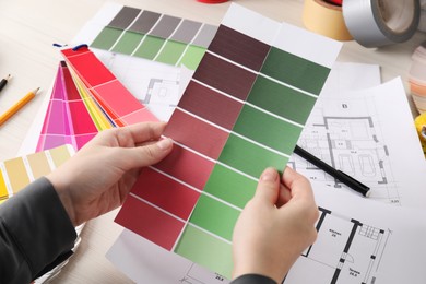 Photo of Designer with color selection chart working on house project at table, closeup