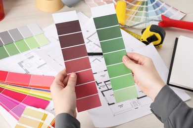 Photo of Designer with color selection chart working on house project at table, closeup