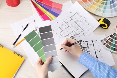 Photo of Designer with color selection chart working on house project at table, closeup