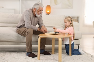 Photo of Grandpa and his granddaughter playing checkers at table indoors