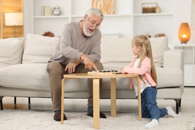 Photo of Grandpa and his granddaughter playing checkers at table indoors